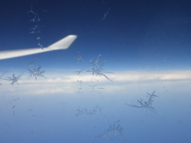 Eine Tragfläche durch ein teils vereistes Flugzeugfenster betrachtet.