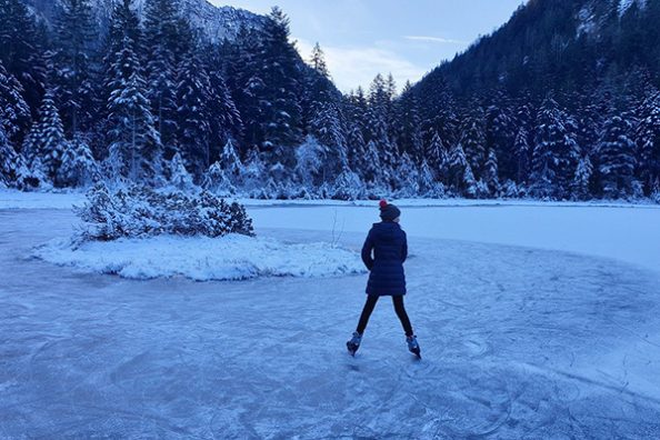 Eine Schlittschuhläuferin in winterlicher Landschaft als Symbolbild.