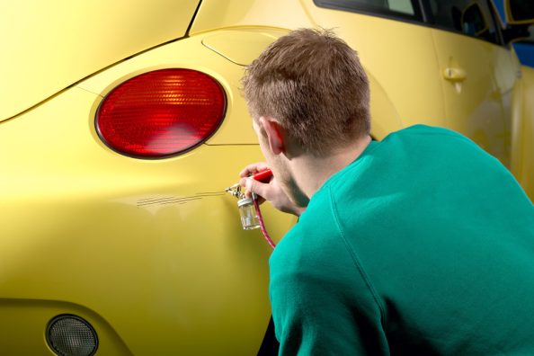 Mann kniet vor einem gelben Auto und behebt einen Lackschaden.