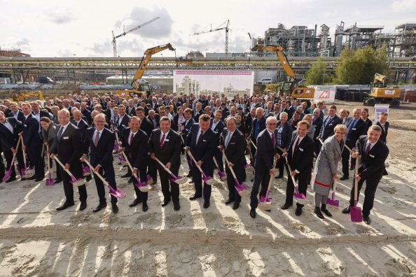 Männer und Frauen mit Spaten vor einer Baustelle.