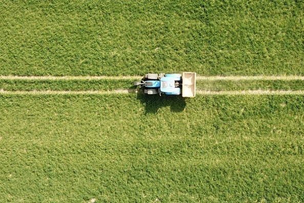 Ein Traktor mit Düngerbehälter aus der Vogelperspektive auf einem Feld.