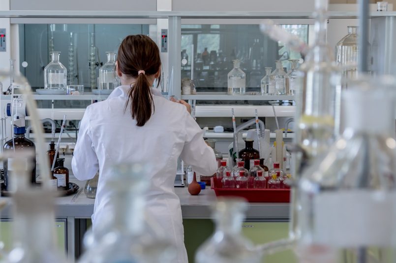 Symbolbild: Frau in einem Labor mit verschiedenen Glas- und Kunststoffbehältern.