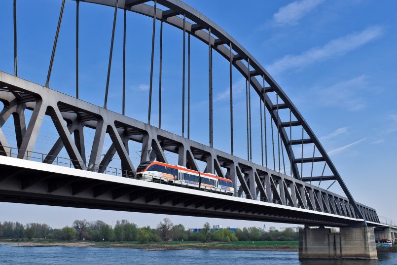 Rote Bahn fährt über eine Eisenbahnbrücke über einem Fluss.