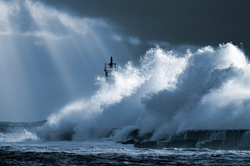 Eine sehr große Welle trifft bei stürmischem Wetter auf einen Leuchtturm.